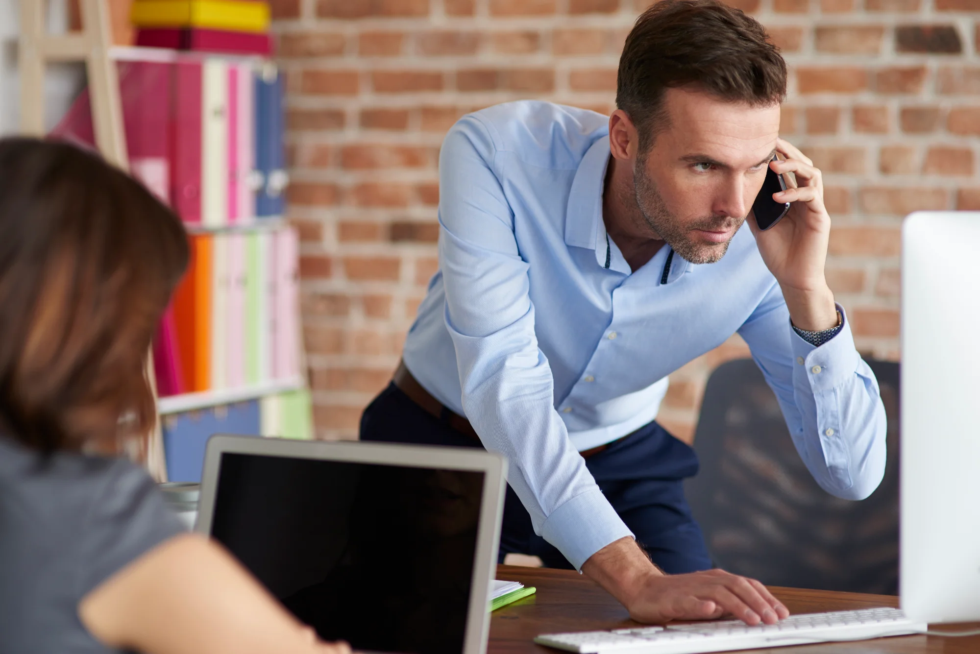 An employee works through a hands-on problem at a desk while a colleague watches and offers guidance